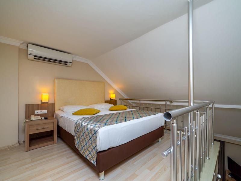 Nowoczesny pokój hotelowy z łóżkiem, lampkami nocnymi i klimatyzacją pod skośnym sufitem.