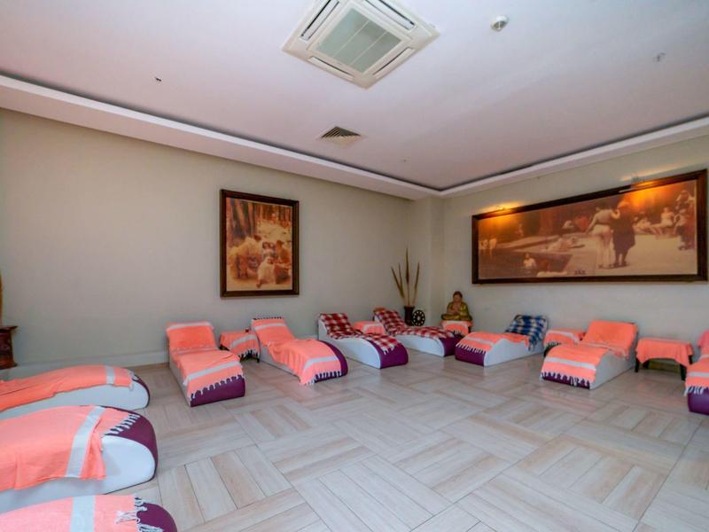 Pokój relaksacyjny z wieloma leżakami, udekorowany poduszkami i roślinami na ścianach.