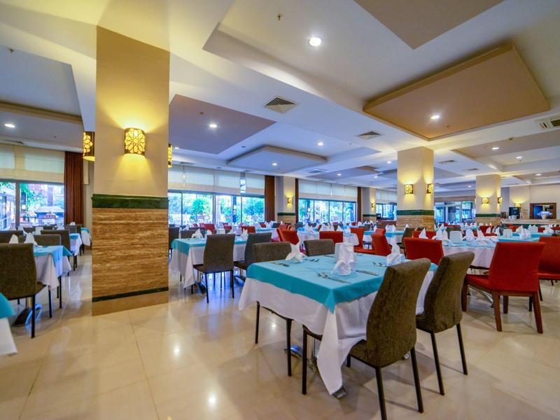 Przestronna, jasna sala jadalna z nakrytymi stołami i krzesłami w kolorach czerwonym, brązowym i niebieskim.