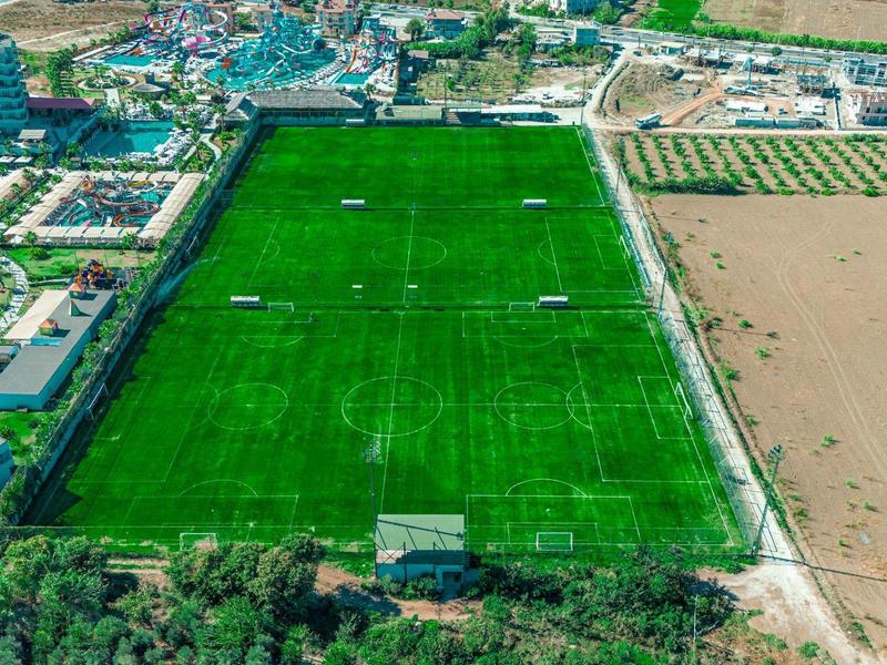 Widok z lotu ptaka na duże zielone boisko piłkarskie obok terenów mieszkalnych i rolniczych.