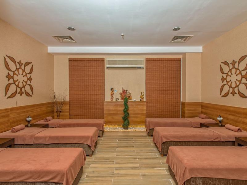 Salle de massage calme avec six lits, tons chauds de bois et motifs décoratifs aux murs.