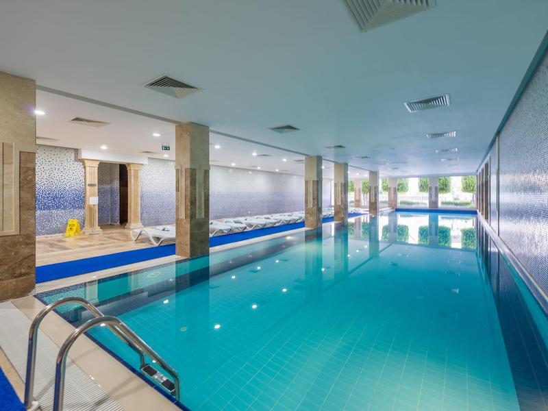 Une piscine intérieure lumineuse et moderne avec des carreaux bleus et plusieurs colonnes.