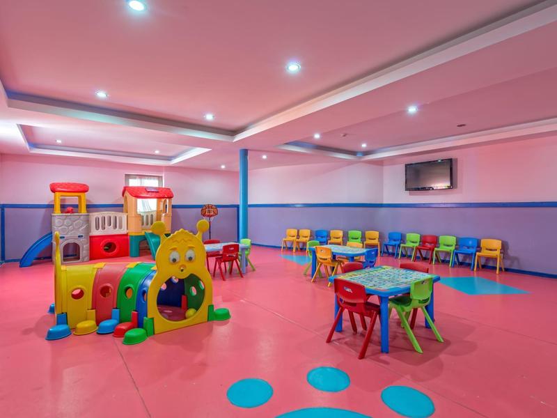 Salle de jeux pour enfants colorée avec structure d'escalade, tables et chaises dans un hôtel.