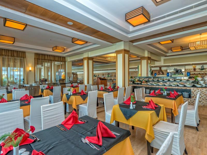 Salle à manger lumineuse avec tables dressées, nappes noires et jaunes, et serviettes rouges.