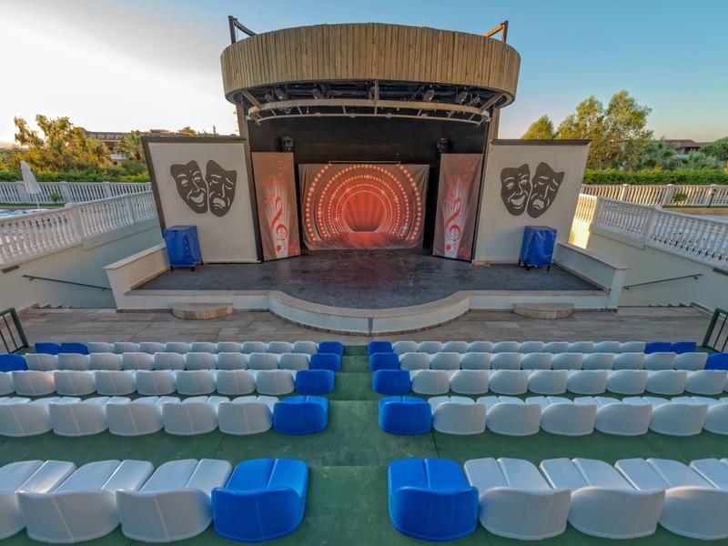 Scène en plein air avec des sièges blancs et bleus, entourée de barrières et d'arbres en arrière-plan.