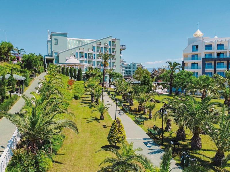Vue sur des bâtiments d'hôtel modernes et un jardin bien entretenu avec des palmiers et des allées sous un ciel bleu.