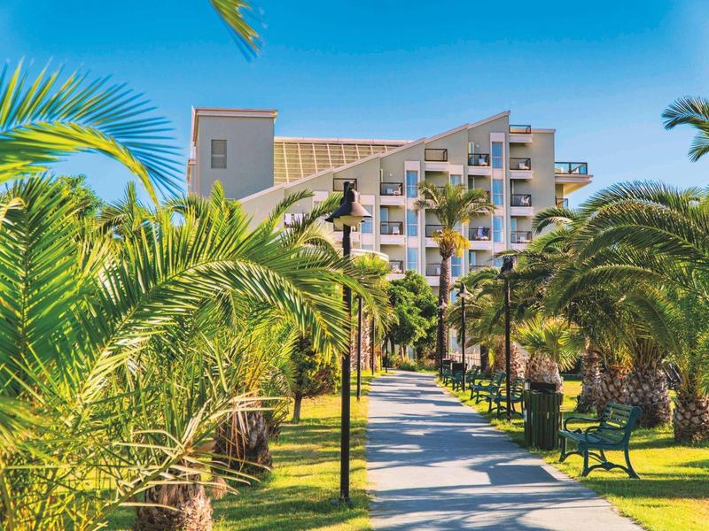 Un hôtel derrière une allée bordée de palmiers sous un ciel bleu.