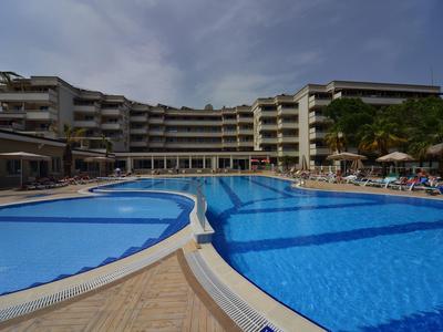 Velký hotelový bazén s několika částmi a lehátky vedle vícepodlažní hotelové budovy.