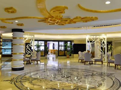 Prostorná hotelová lobby s ozdobnou mramorovou podlahou, pohodlnými křesly a dekorativními sloupy.