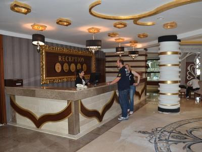 Hotelová recepce s hostem a recepční, moderní interiér se sloupem a kobercem.