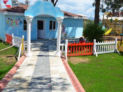 Cesta vede k světle modré budově s malou zahradou a barevnými ploty za slunečného dne.