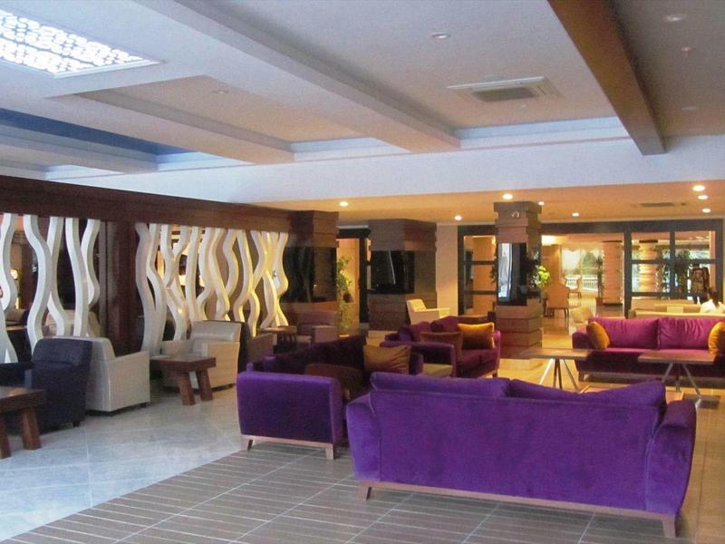 Moderní hotelová lobby s fialovými pohovkami, posezením a dekorativními stěnovými prvky.