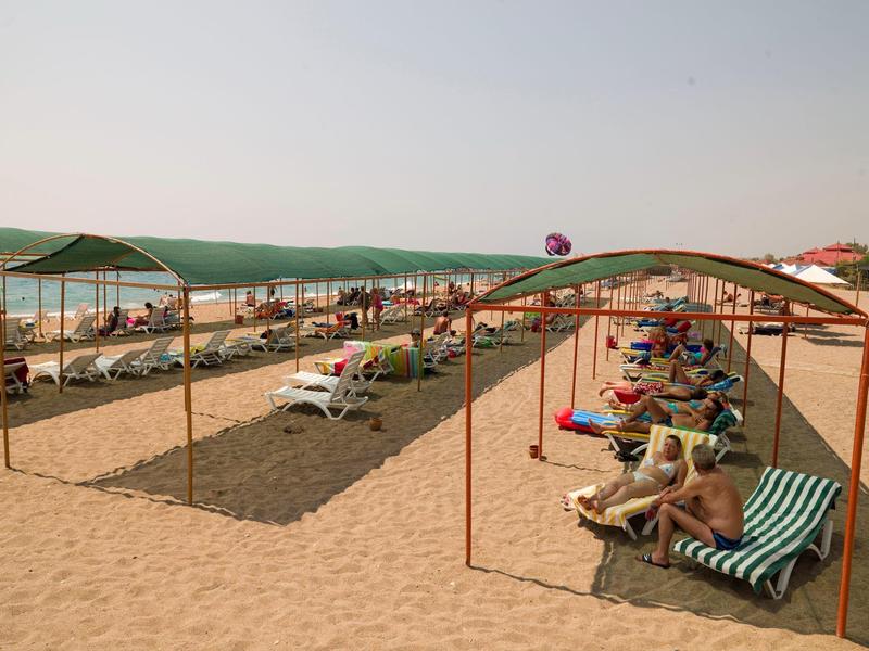 Pláž s lehátky, slunečníky a lidmi odpočívajícími na slunci.