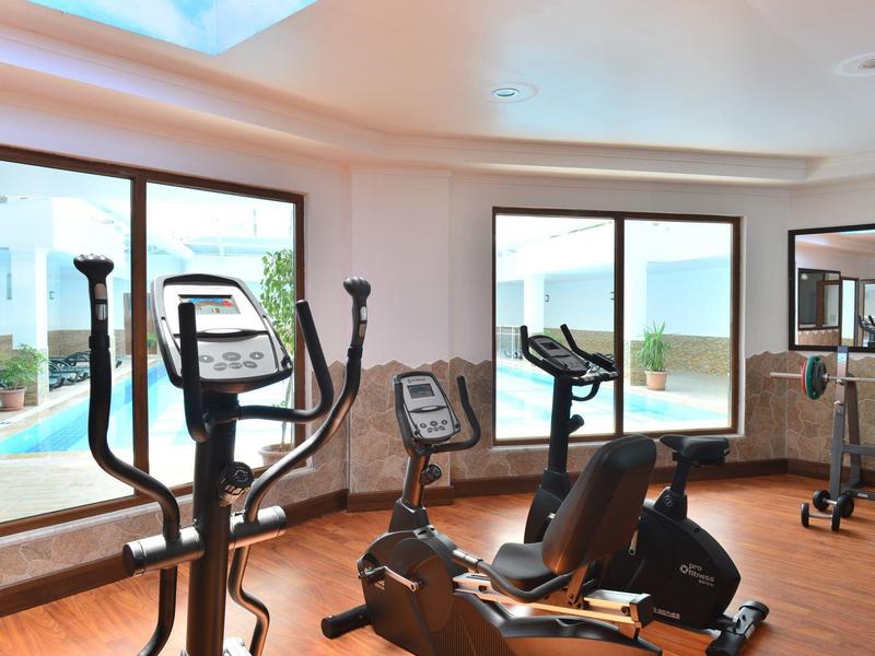 Světle vybavená posilovna s různými tréninkovými přístroji a výhledem na bazén a moře.