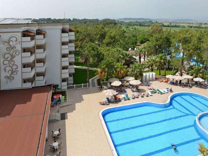 Hotel s velkým bazénem, slunečníky a zalesněnou oblastí v pozadí.