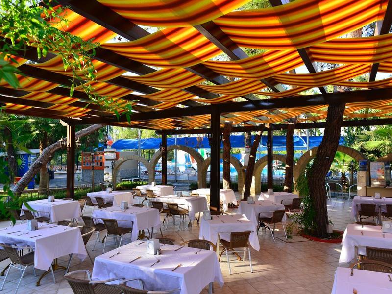 Zastřešená venkovní restaurace s bílými ubrusy na stolech a výhledem na bazén.