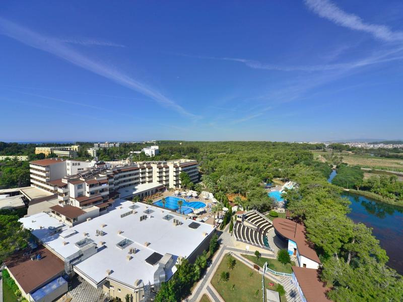 Pohled na hotelový resort s několika bazény, hojností zeleně a modrou oblohou.