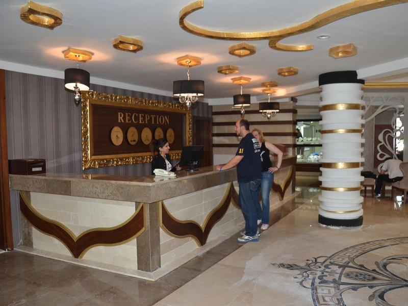 Hotelová recepce s hostem a recepční, moderní interiér se sloupem a kobercem.