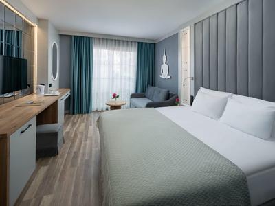 Moderní hotelový pokoj s velkou postelí, psacím stolem a pohodlným posezením u okna.