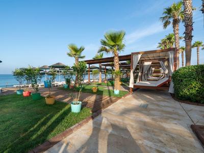Strandhotel mit Liegen, Sonnenschirmen und Palmen an der Promenade bei klarem Himmel.