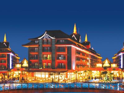 Beleuchtetes Hotelgebäude mit Zinnen und Pool vor blauem Nachthimmel.