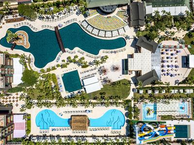 Vogelperspektive eines großen Hotels mit mehreren Pools und viel Grünfläche.