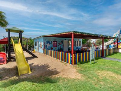 Bunter Spielplatz mit Rutsche und Sandbereich vor einem bunten Gebäude im Freien.