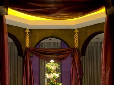 Elegant indoor fountain under decorative arch with draped curtains and floral centerpiece.