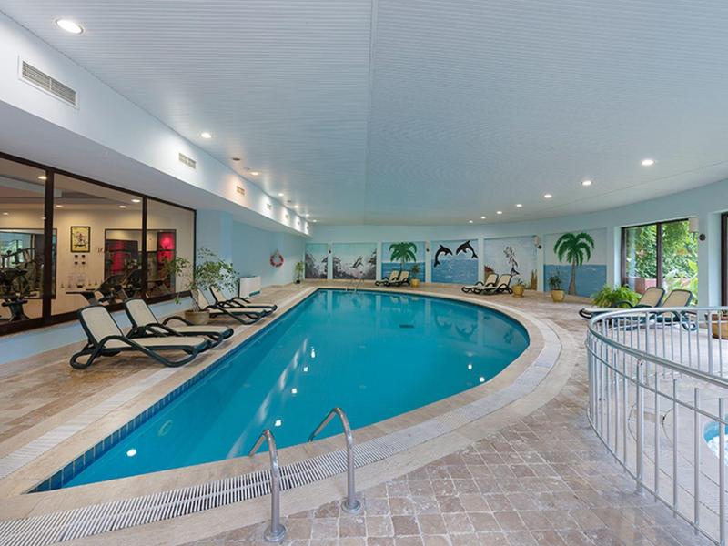 Indoor hotel pool area with loungers, glass windows, and tiled floor in a spacious setting.