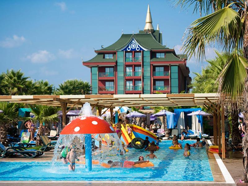 Hotel pool area with colorful slides, umbrellas, and children playing under a clear sky.