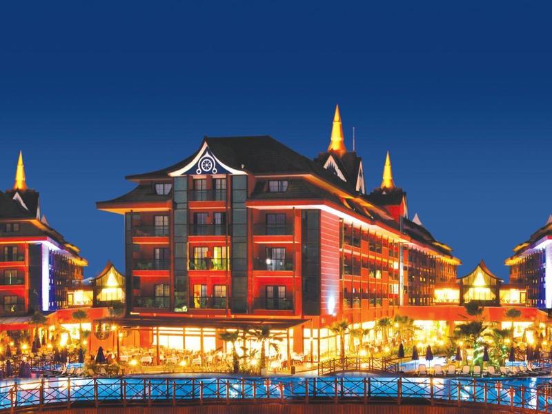 Luxurious hotel resort illuminated at night with a large swimming pool in front under a clear sky.