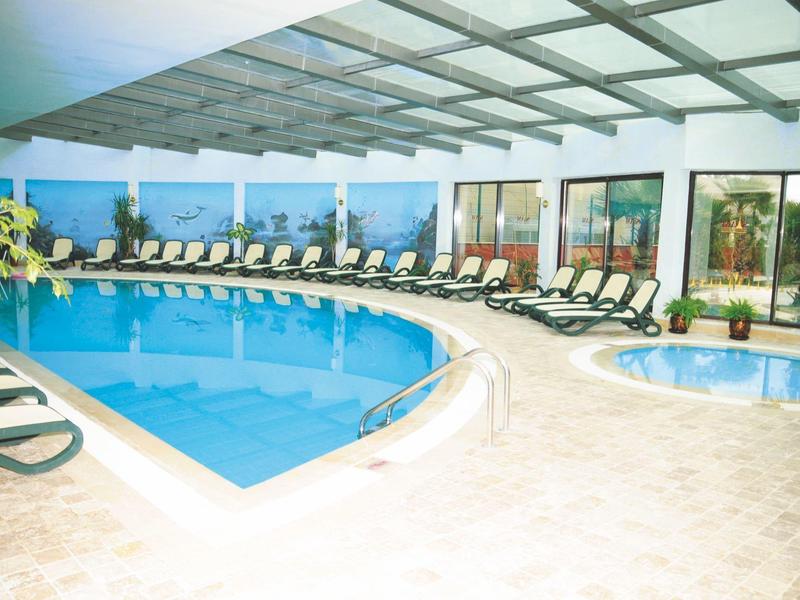 Indoor pool area with lounge chairs and a hot tub, surrounded by large windows and a glass ceiling.