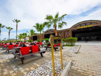 Outdoor seating area with red benches in front of a tropical-style restaurant under a partly cloudy sky.