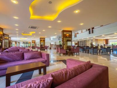 Moderna hall d'hotel con divani viola, tavoli, area bar e illuminazione gialla sul soffitto.