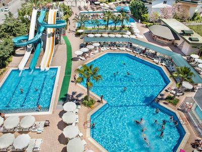 Bazény a vodní skluzavky obklopené palmami a slunečníky v hotelovém komplexu.