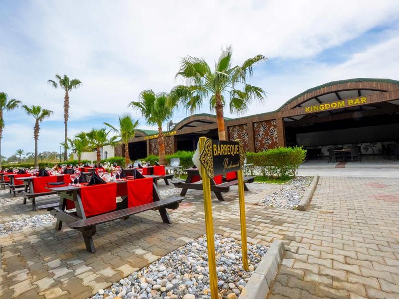 Outdoor seating area with red benches in front of a tropical-style restaurant under a partly cloudy sky.