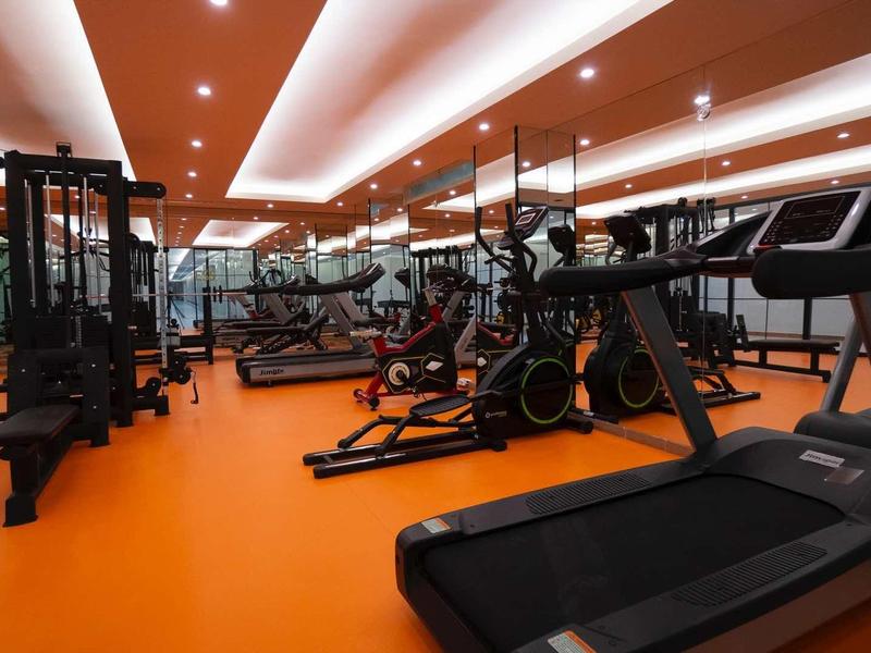 Modern gym with orange floor, treadmills, exercise bikes, and weight machines under bright lights.