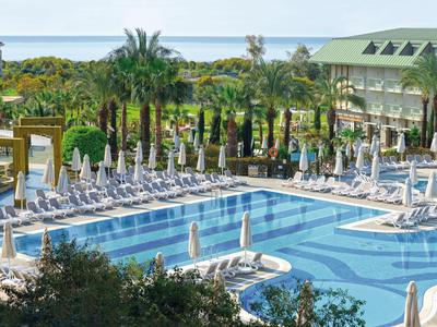 Großer Hotelpool mit Liegestühlen, Palmen und Meerblick bei klarem Himmel.