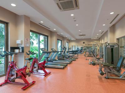 Fitnessraum mit modernen Geräten und großen Fenstern mit Blick auf Grünflächen.