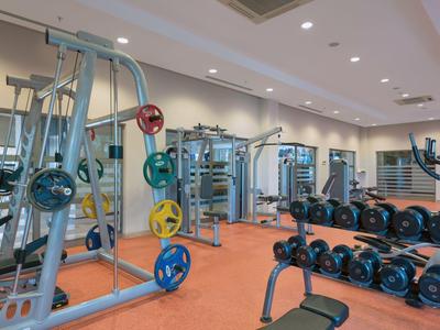 Moderner Fitnessraum mit verschiedenen Kraftgeräten und Hanteln vor einem Spiegel