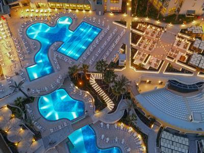 Přehled několika zářících modrých hotelových bazénů v noci s okolními budovami a cestami.