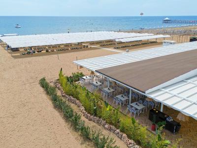 Strand mit Sand, überdachten Sitzbereichen und ruhigem Meer im Hintergrund.