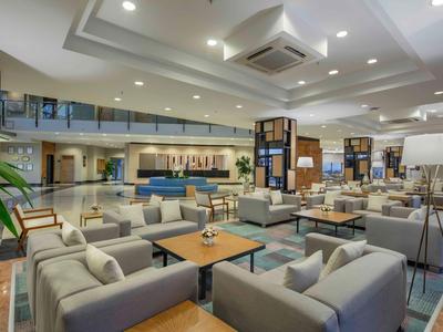 Moderne Hotellobby mit Sitzecken, Tischen und Deckenbeleuchtung in hellem Ambiente.