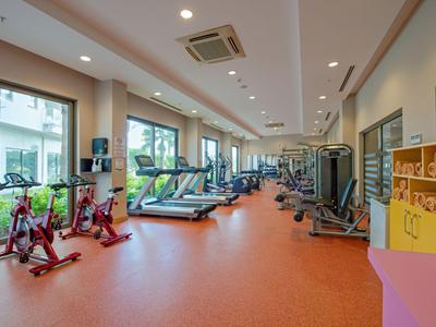 Moderner Fitnessraum mit Cardio- und Kraftgeräten, großen Fenstern und rotem Bodenbelag.