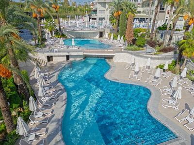 Hotelpool mit blauen Wasserflächen, weißen Liegestühlen und Palmen im Außenbereich.