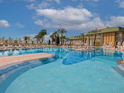Ein großer Hotelpool mit Sonnenschirmen, Liegestühlen und Palmen unter blauem Himmel.
