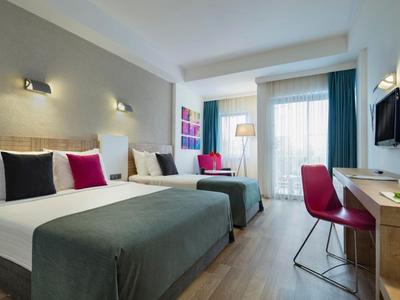 Modernes Hotelzimmer mit zwei Einzelbetten, Schreibtisch und großen Fenstern.