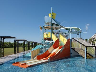 Wasserrutsche mit orangefarbenen Bahnen in einem Pool neben einem Hotelgebäude.