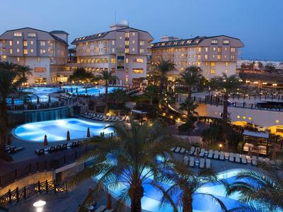 Luxusní hotel s několika osvětlenými bazény a palmami za soumraku.