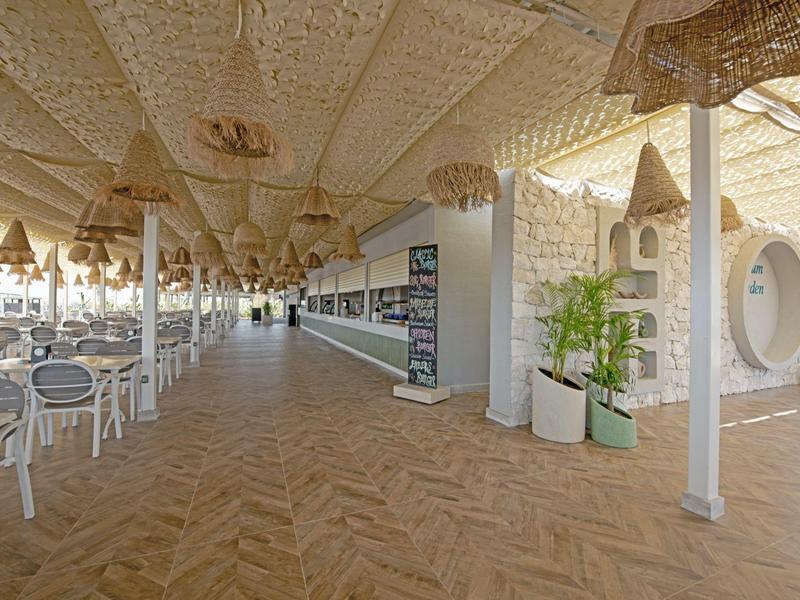 Otevřený jídelní prostor s bílými židlemi, dřevěnou podlahou a dekorativním stropem.